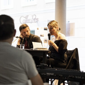 Autor:innen Alexandru Bulucz und Frieda Paris und Musiker Ben Lageder im Fenster der Galerie Ferner bei den Galeriedialogen