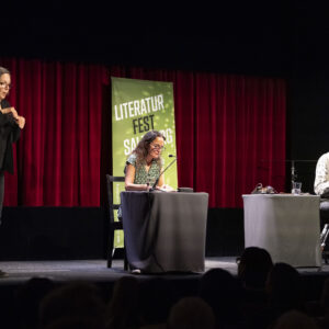 Autorin Elke Laznia, Musiker Albin Paulus und eine ÖGS-Dolmetscherin auf der Bühne bei der Eröffnung des 17. Literaturfest